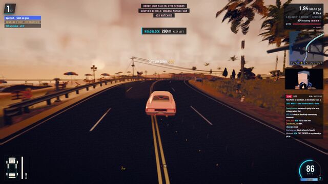 An orange muscle car on a palm-lined coast road at Vela Point at sundown, with a roadblock warning 260 m ahead (full size, 1920 × 1080)